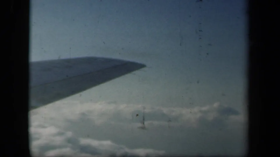 1941 home-movie frame from an airplane window, showing the wing tip against blue sky and clouds below.