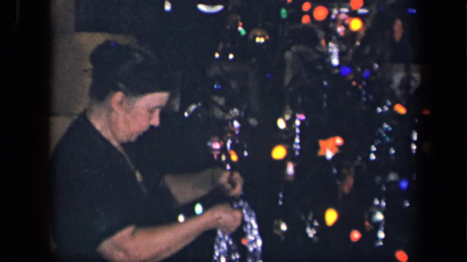 In a 1942 Sebring, Ohio home movie frame, a woman with a bun handles silver tinsel near a glowing Christmas tree.