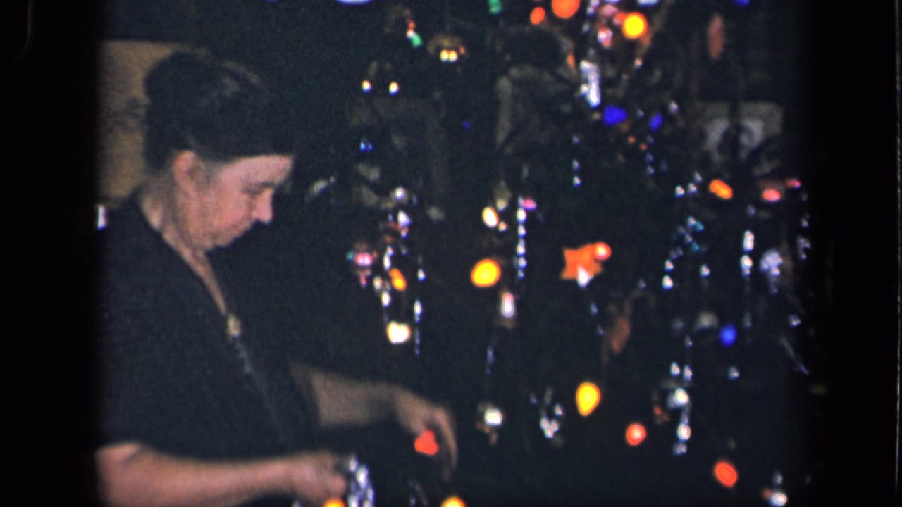 A woman in a dark dress looks down as she handles tinsel beside a lit Christmas tree in a private Sebring, Ohio interior.