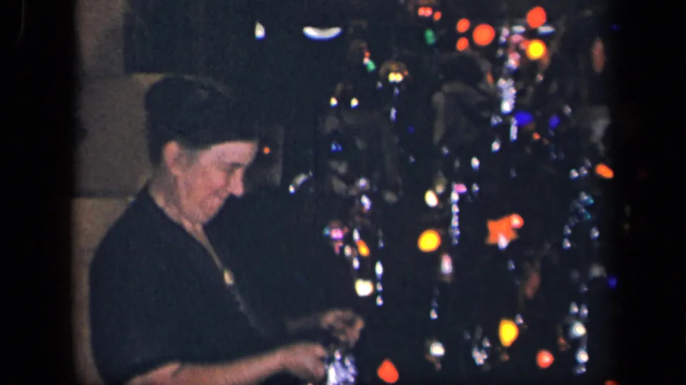 In the Sebring, Ohio holiday scene, the woman lowers her gaze while holding a reflective ornament or tinsel near the decorated tree.