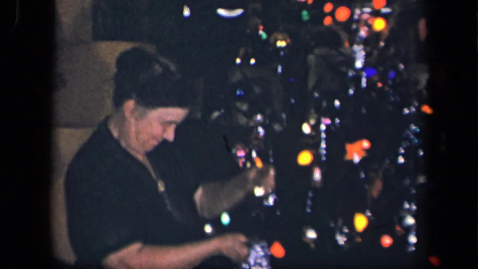 An older woman smiles faintly as she works near a brightly lit Christmas tree in this 1942 Sebring, Ohio home-movie frame.