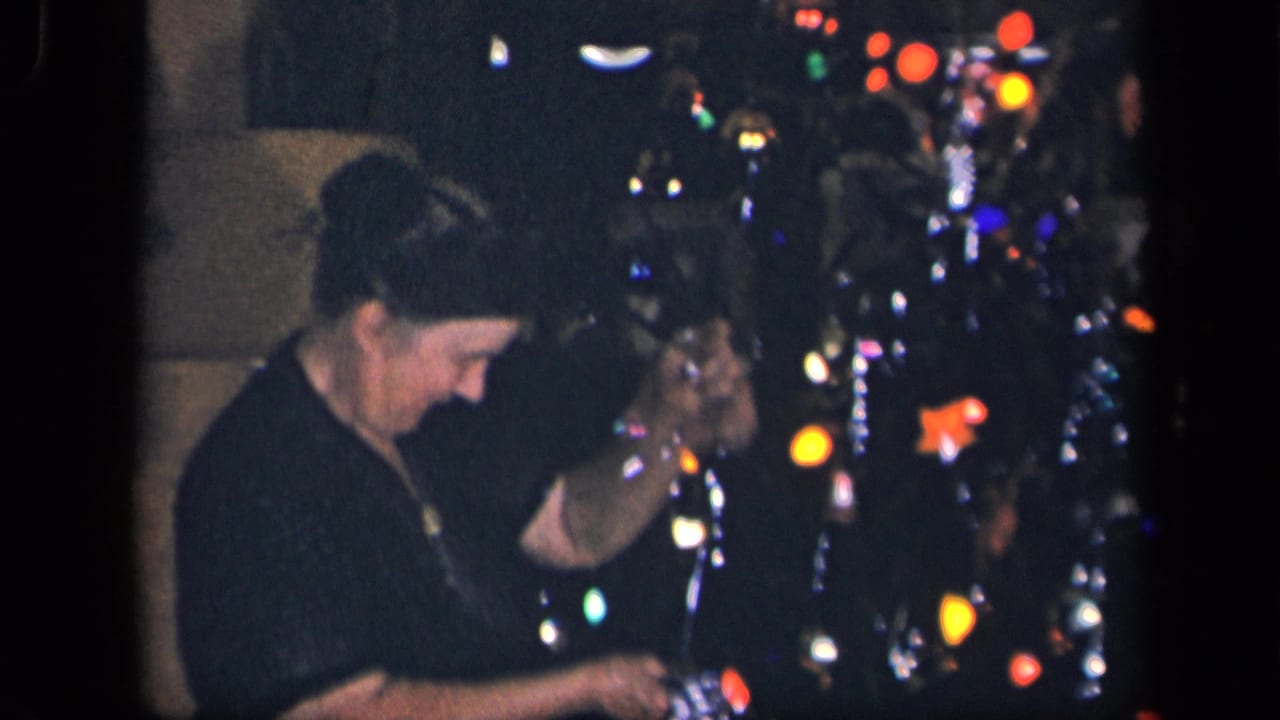In supported 1942 Sebring, Ohio home-movie footage, a woman stands beside a glowing Christmas tree and handles decorations.