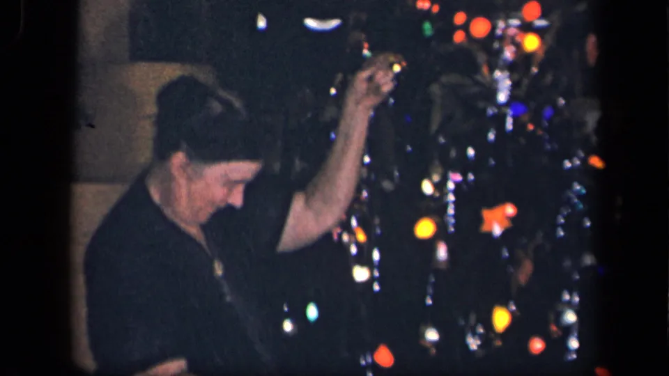 A woman in the 1942 Sebring, Ohio home-movie clip lifts her hand while working near a lit, ornamented Christmas tree.