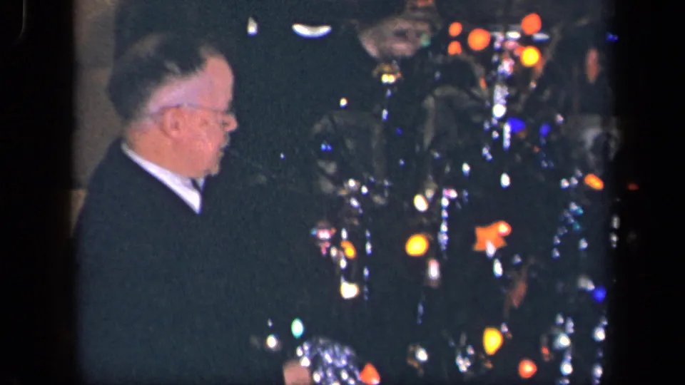 The elderly man appears in profile beside the decorated Christmas tree, with tinsel strands and colored lights visible in the 1942 home interior.