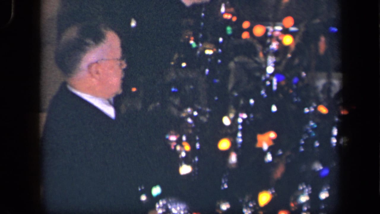 In a 1942 Sebring, Ohio home-movie frame, an older man in glasses faces a decorated Christmas tree with colored lights and tinsel.
