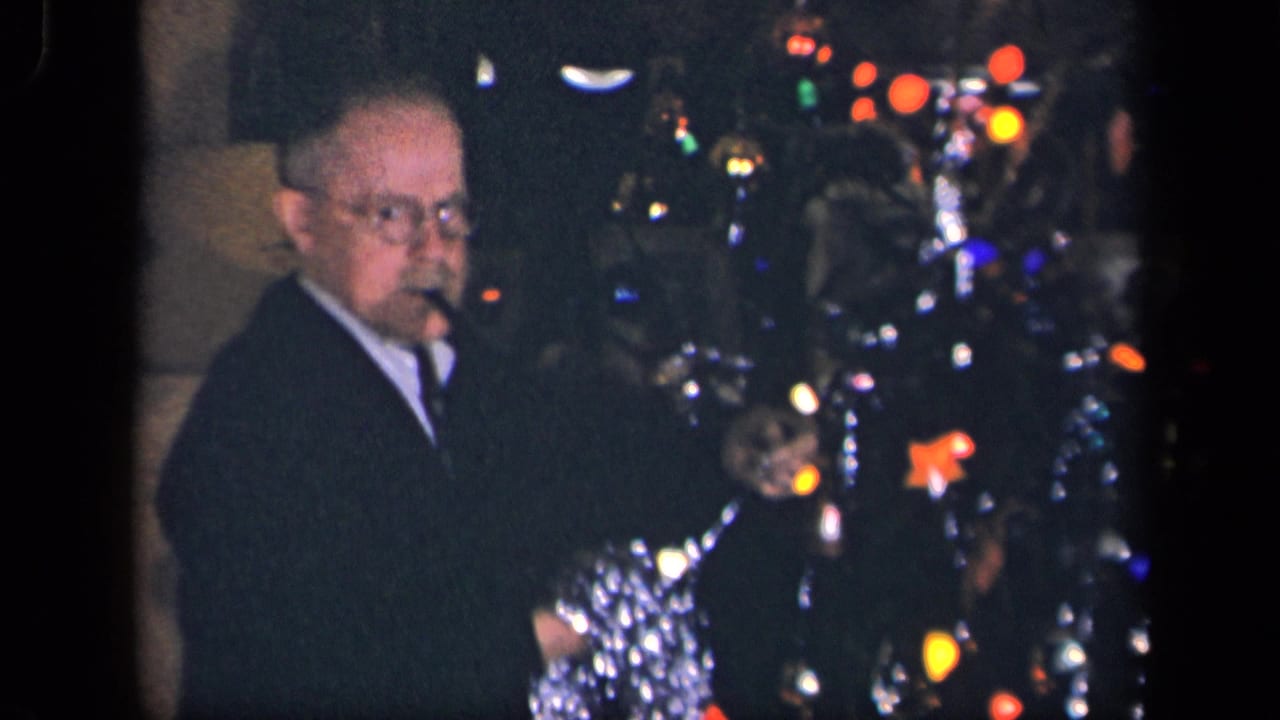 In a 1942 Sebring, Ohio home movie frame, an older man with glasses stands near a decorated Christmas tree in a dim room.