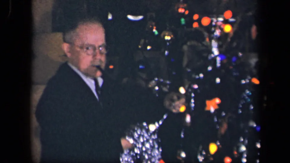 In a 1942 Sebring, Ohio home movie frame, an older man with glasses stands near a decorated Christmas tree in a dim room.