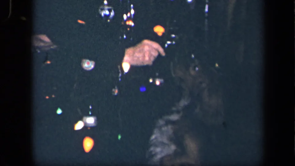 1942 Sebring, Ohio home-movie frame showing a lit Christmas tree, a partially visible person, and a small dog in a dark room.