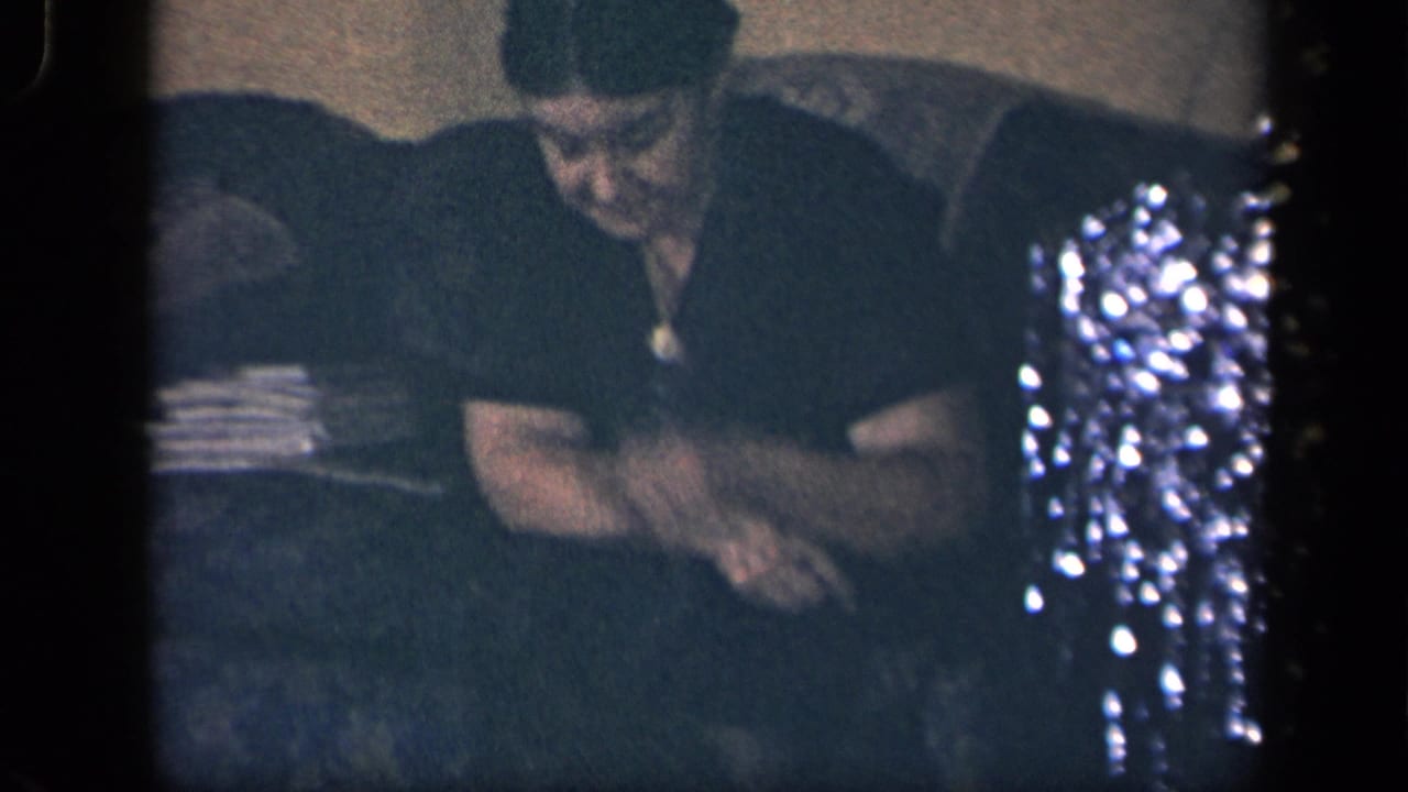 1942 Sebring, Ohio frame of a woman seated on a couch near tinsel, leaning toward a small dog in a private interior.