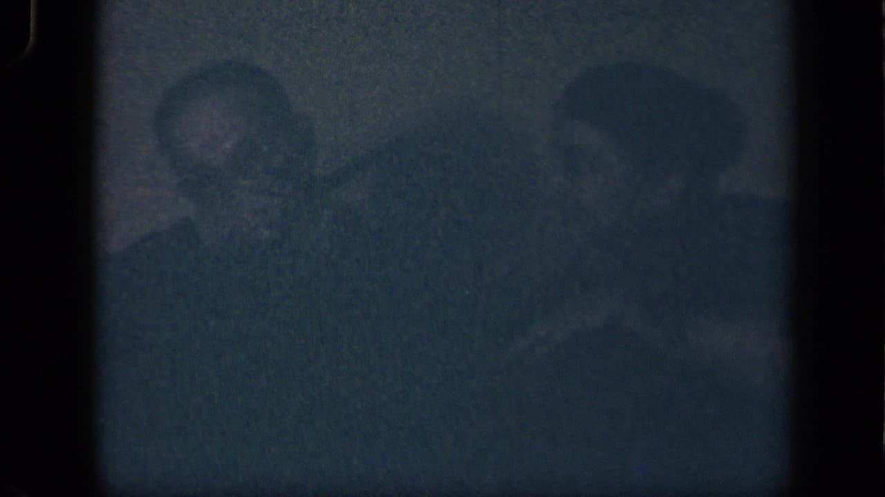 Low-light 1942 Sebring, Ohio 8mm frame showing two seated adults, the man at left partly visible with a pipe and a woman beside him.