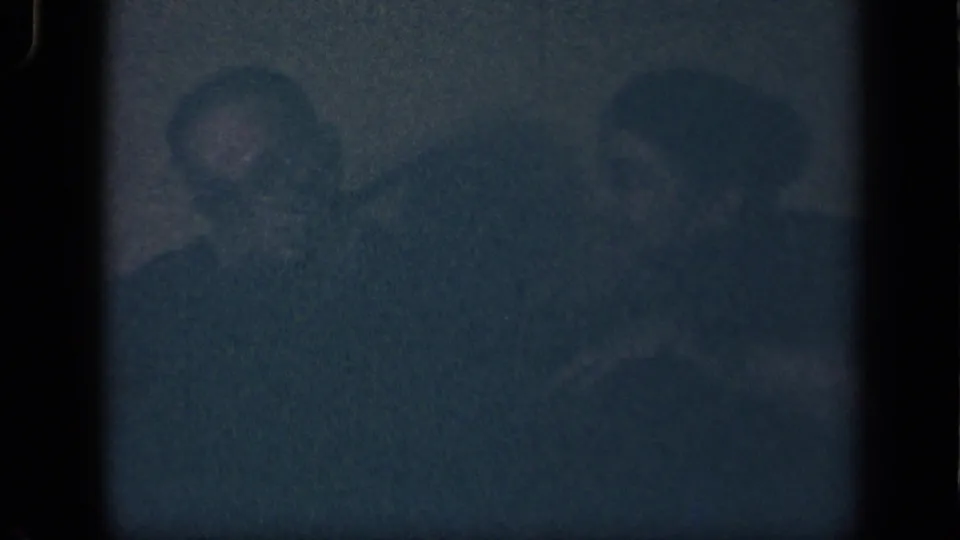 Low-light 1942 Sebring, Ohio 8mm frame showing two seated adults, the man at left partly visible with a pipe and a woman beside him.