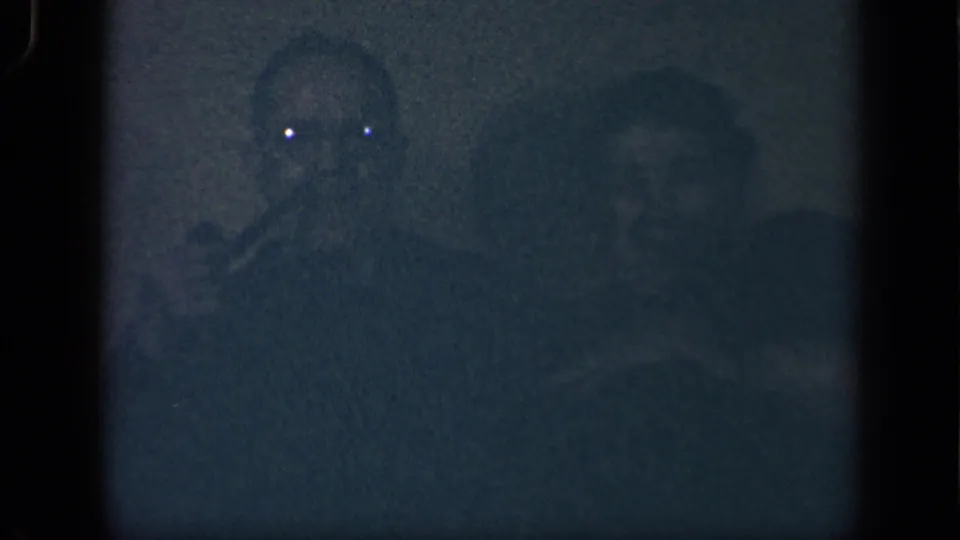 Grainy 1942 Sebring, Ohio home-movie frame with a man holding a pipe beside a seated woman in very low light.