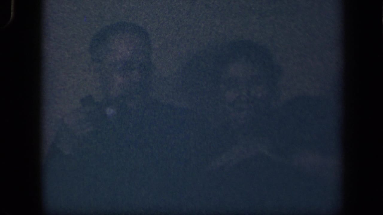 In the supplied 1942 Sebring, Ohio home-movie context, two adults appear in a dim interior, partly obscured by grain and shadow.
