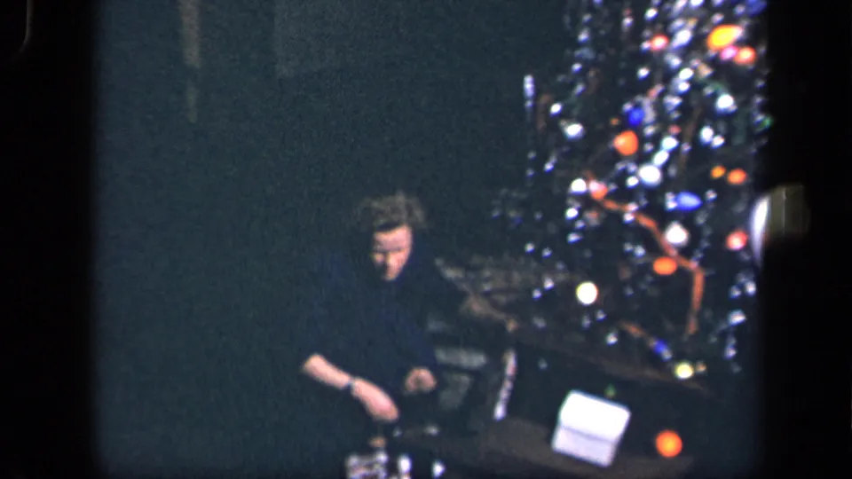 A seated adult appears beside a decorated Christmas tree in the 1942 Sebring, Ohio home-movie setting, with gifts visible near the base.