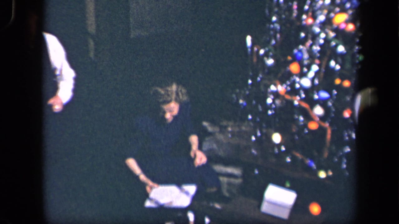 The seated woman leans over wrapping paper near the illuminated Christmas tree in the Sebring, Ohio holiday home movie.