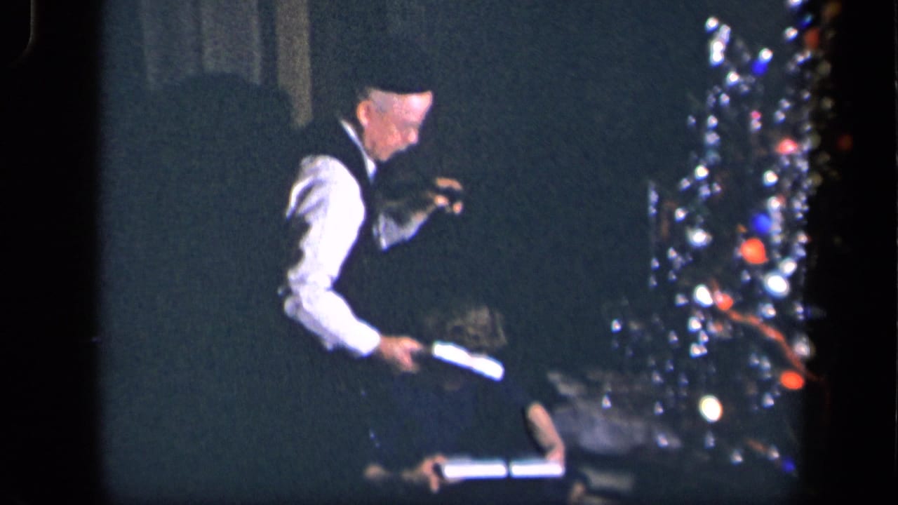 The man holds a wrapped parcel while a woman sits on the floor near the Christmas tree in the Sebring, Ohio interior.
