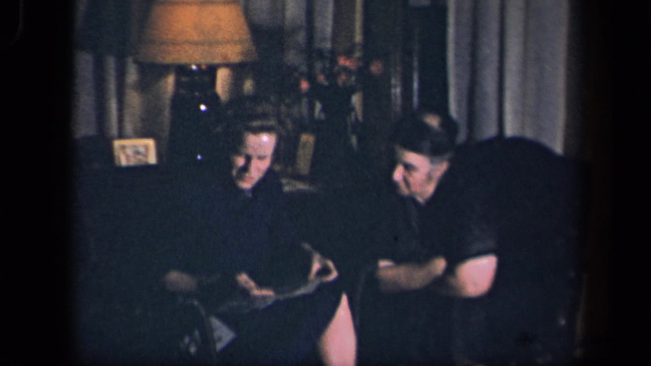 In this 1942 Sebring, Ohio home-movie frame, a woman in a dark dress sits beside a man while looking down at a card in a dim living room.