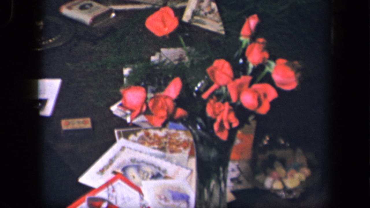 Bouquet of red roses with scattered cards, papers, and a bowl of candy on a dark table.