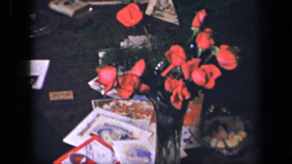 Soft 8mm view from the 1942 Sebring, Ohio clip with red roses, greeting cards, printed papers, and a candy dish on a dark table.