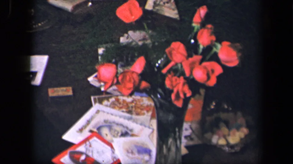Final frame of the Sebring, Ohio 1942 8mm clip showing red roses in a vase, cards and papers, and a glass candy bowl on the tabletop.