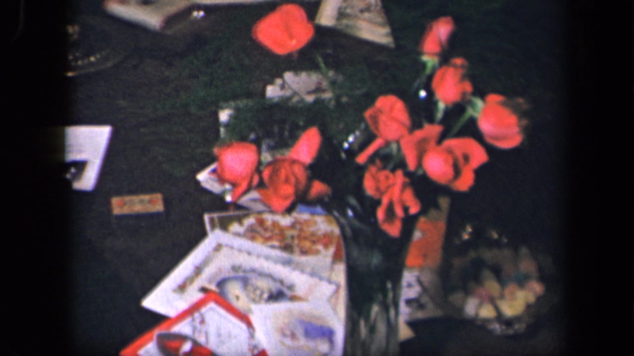 1942 Sebring, Ohio 8mm frame showing red flowers on a dark surface with papers, cards, and small food items nearby.