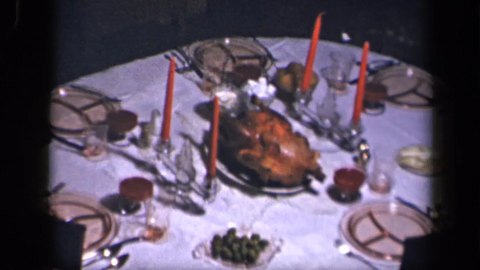 1942 Sebring, Ohio home-movie frame of a formal holiday table with roast turkey, red candles, patterned plates, and glassware.