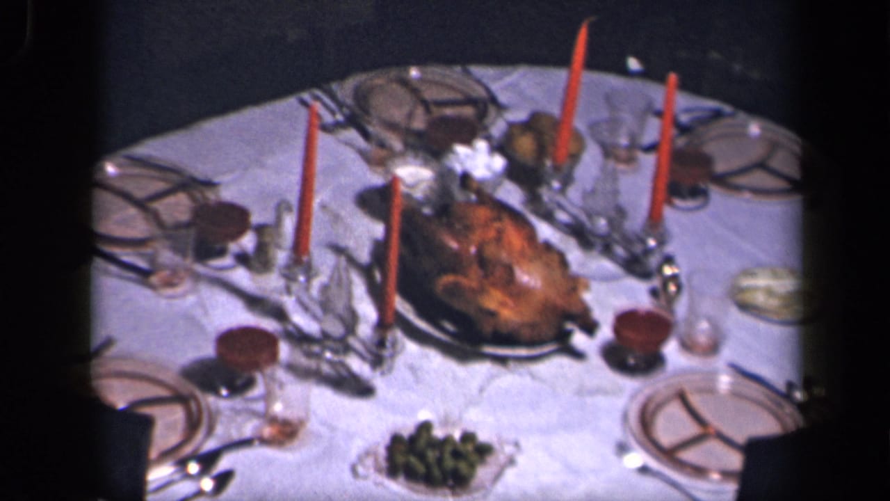 Round Thanksgiving table with roast turkey, red candles, plates and glassware.