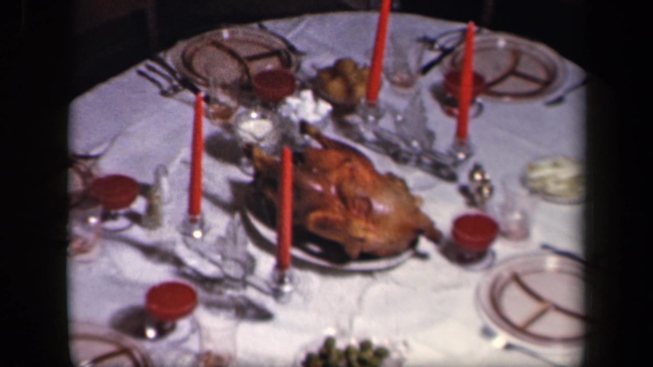 Thanksgiving table with roasted turkey, red candles, white cloth, plates, glassware, and serving dishes.
