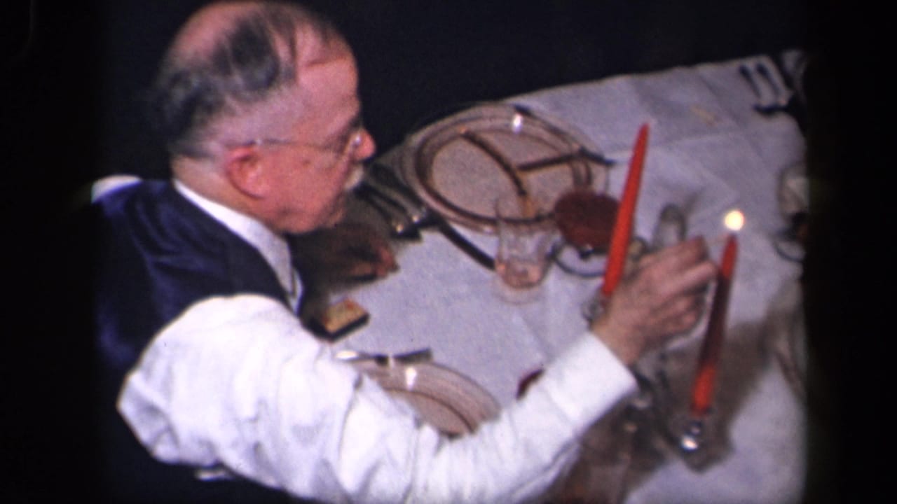 In Sebring, Ohio 1942 footage, an adult man in a vest lights a red candle at a formal dinner table.
