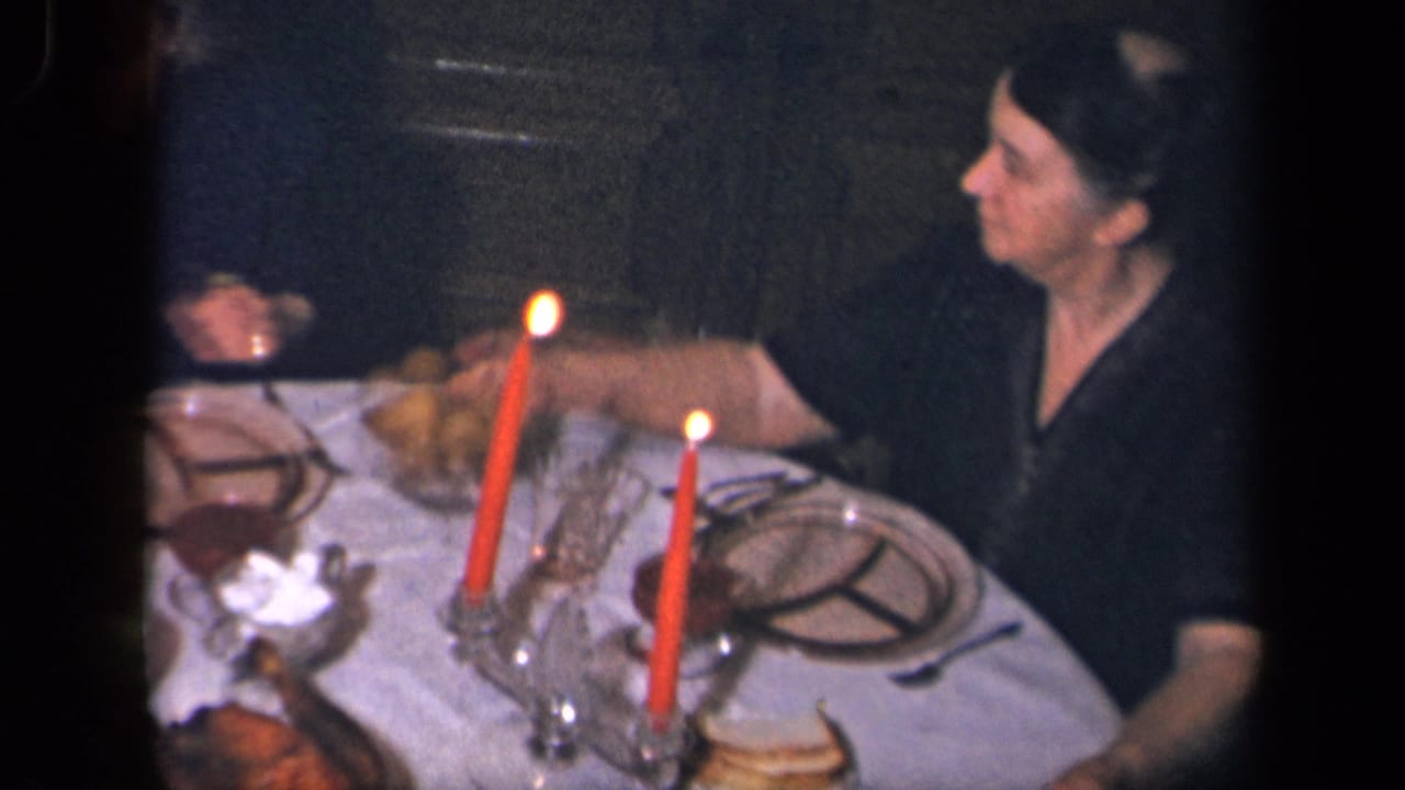 Two women sit at a candlelit dinner table as one reaches toward a dish.