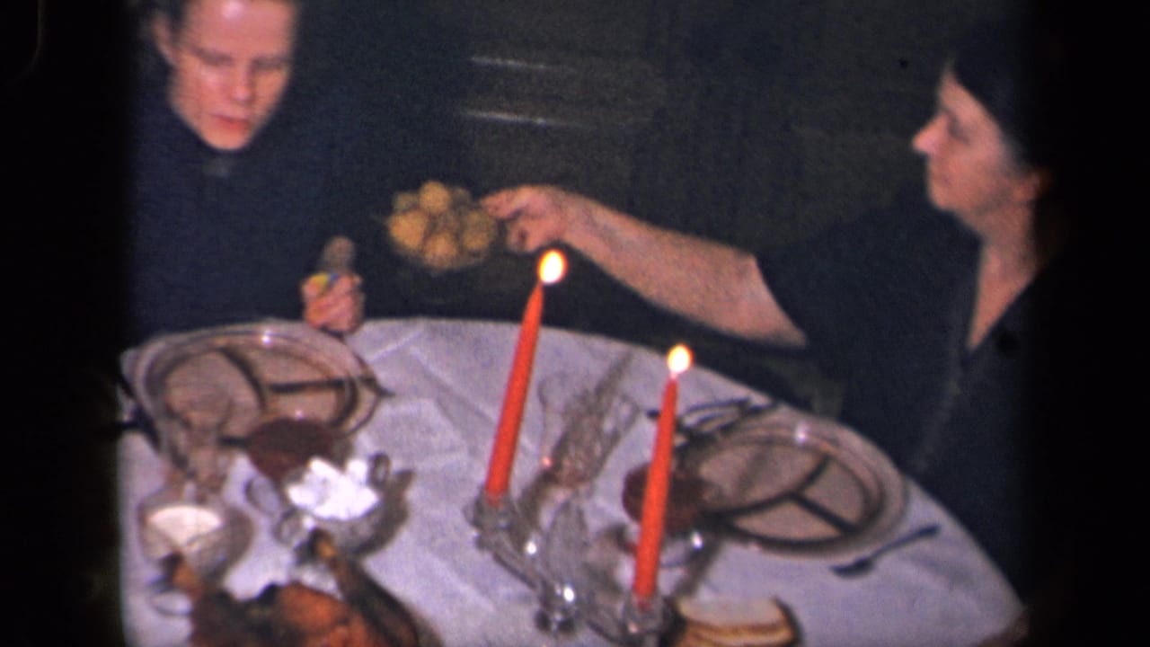 A woman in dark clothing passes a dish across a candlelit dining table in the Sebring, Ohio home-movie footage.