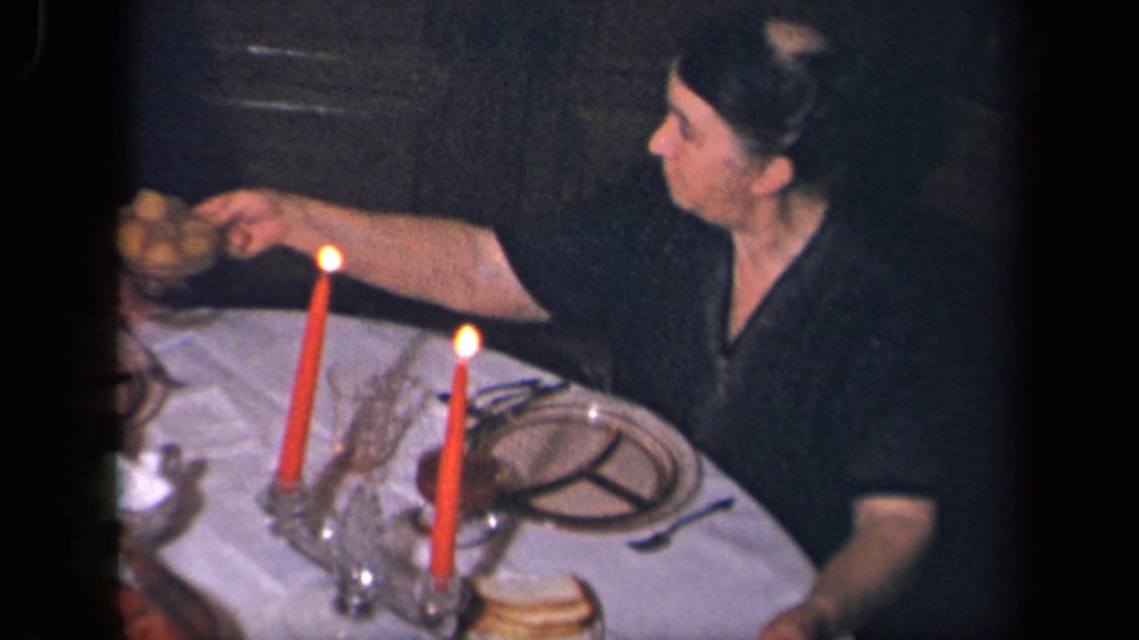 In 1942 Sebring, Ohio home-movie footage, a woman reaches across a white-clothed dinner table with red candles and glassware.