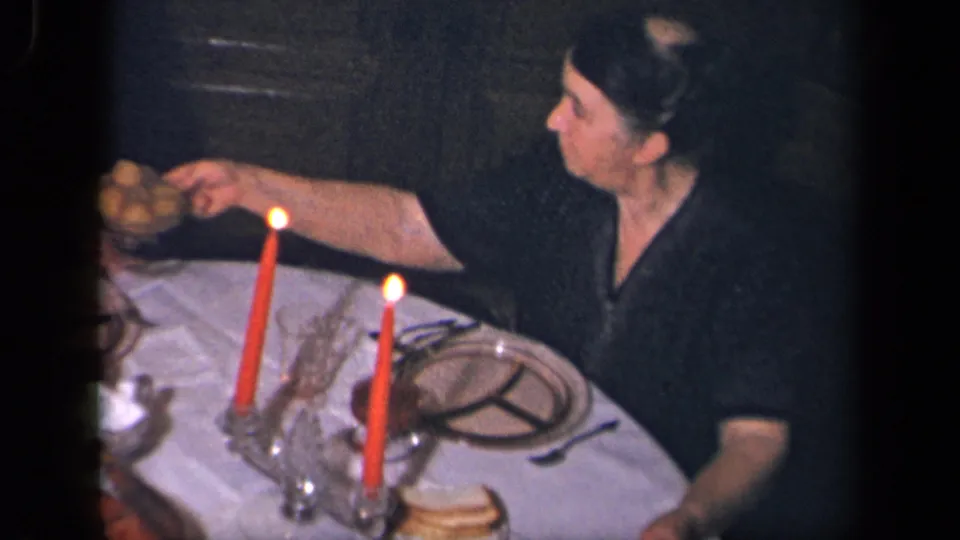 In 1942 Sebring, Ohio home-movie footage, a woman reaches across a white-clothed dinner table with red candles and glassware.