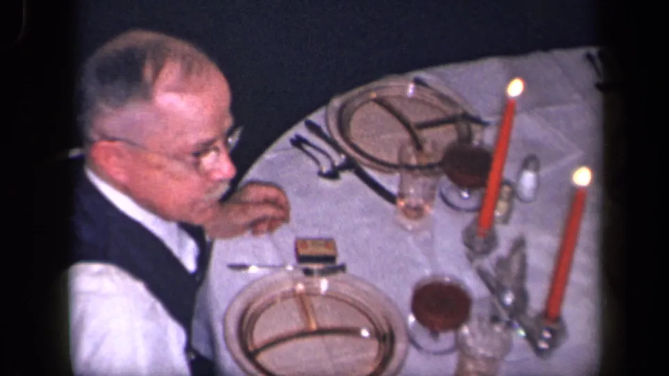 The older man remains at the Sebring, Ohio dinner table, framed above plates, glasses, red candles, and a white tablecloth.