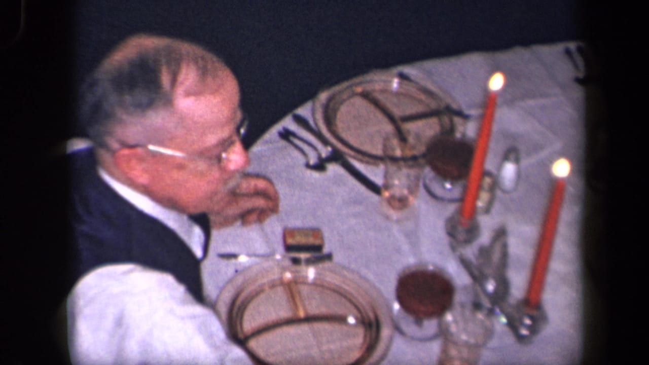 In supported 1942 Sebring, Ohio home-movie footage, a man in glasses sits beside a formal table setting with red candles and dinnerware.