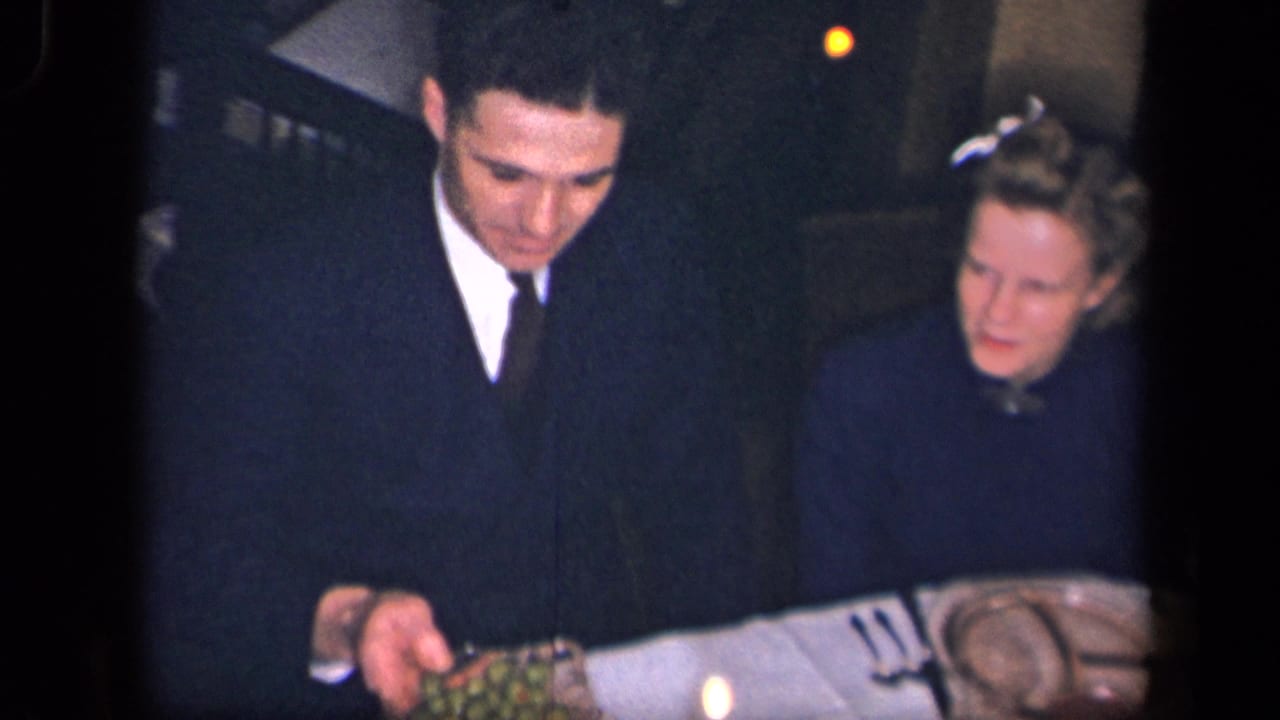 Young man and woman stand or sit near a formal dinner table as food is passed.