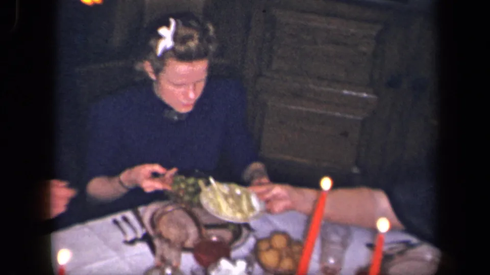 A woman in dark clothing handles the olive dish at a candlelit formal dinner table in supported 1942 Sebring, Ohio footage.