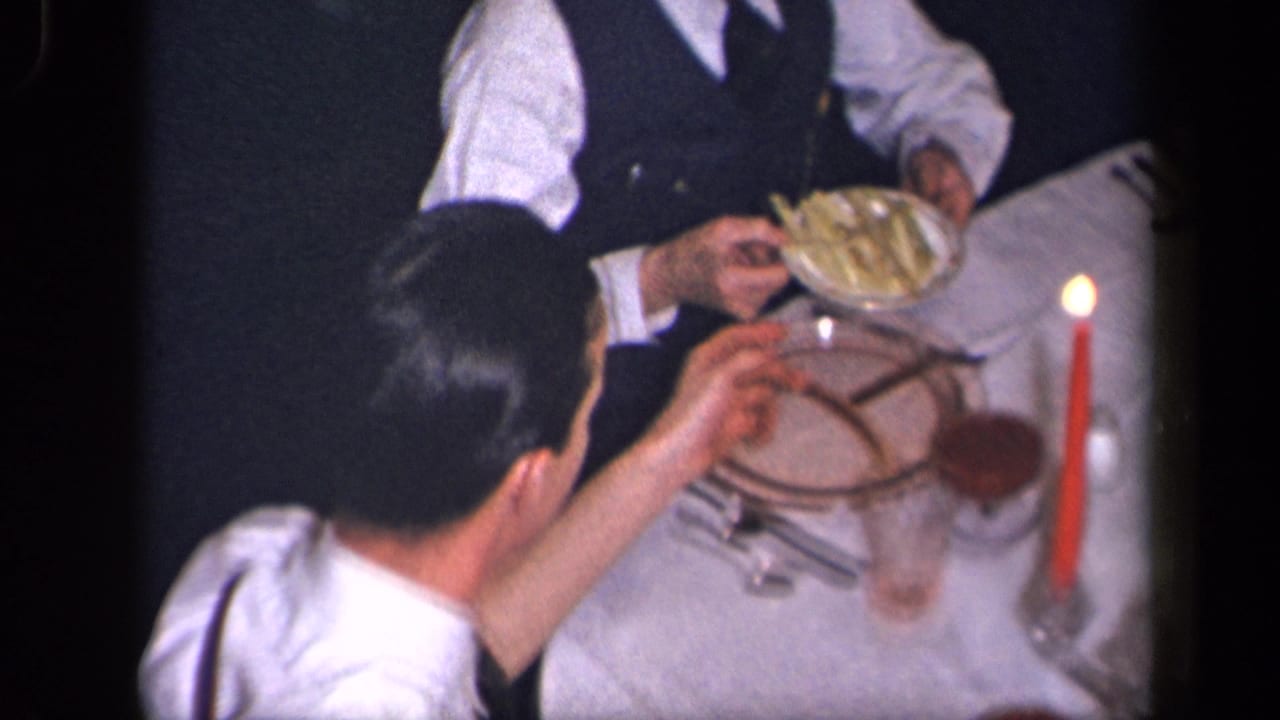 In a 1942 Sebring, Ohio home-movie frame, a man in a white shirt sits at a candlelit table as food is passed nearby.