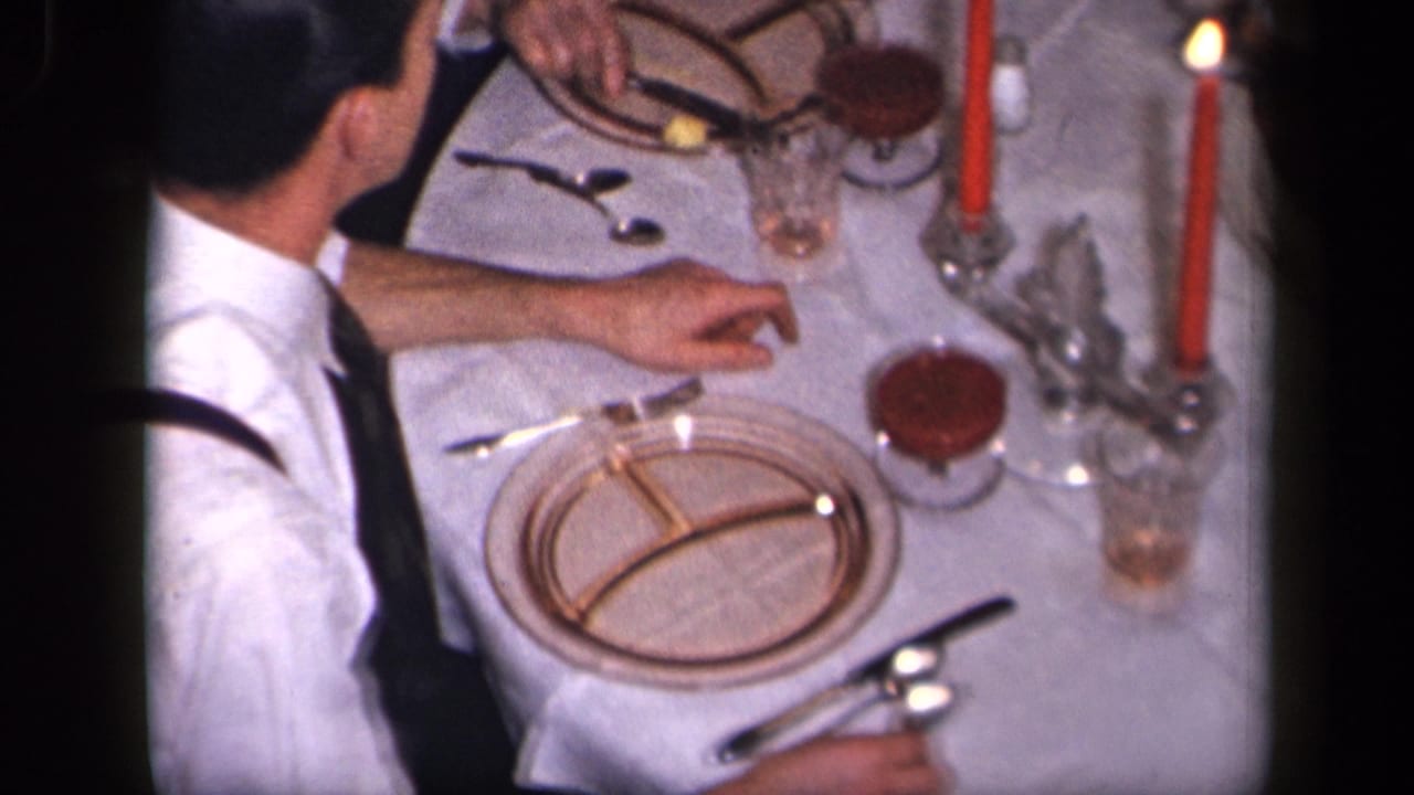 Overhead view of adults seated at a formal table with red candles and dinnerware.