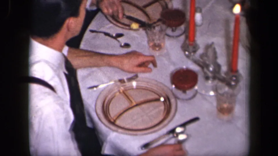 Overhead 1942 Sebring, Ohio home-movie frame showing adults at a formal dinner table with red candles, plates, glassware, and cutlery.
