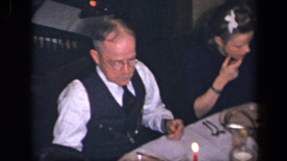 1942 Sebring, Ohio home-movie frame showing an older man in a vest and a woman seated at a formal candlelit dinner.