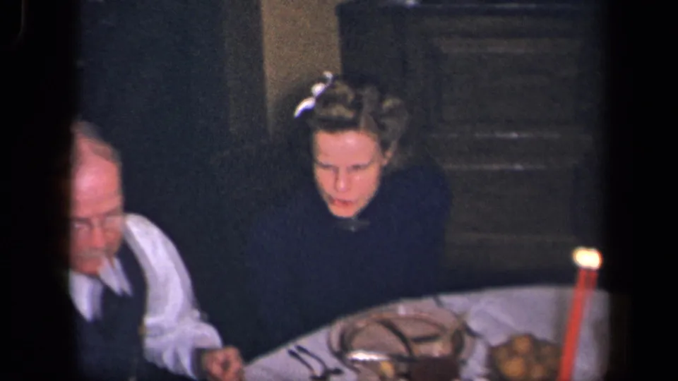1942 Sebring, Ohio frame showing a woman and older man at a formal dinner table with a red candle, dishes, glassware, and potatoes.