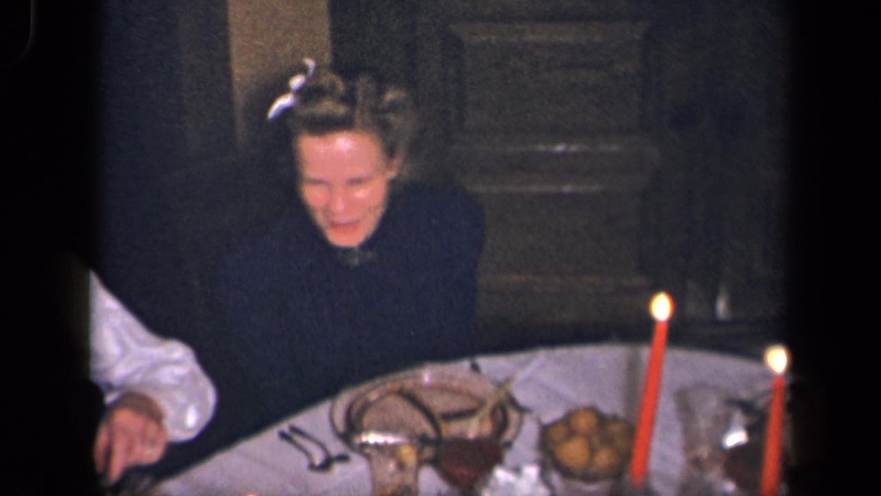 Woman seated at a candlelit dinner table with plates, food, and red candles.