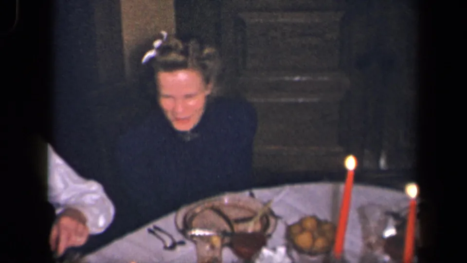 In 1942 Sebring, Ohio home-movie footage, a woman smiles at a candlelit dinner table with food and serving dishes visible.