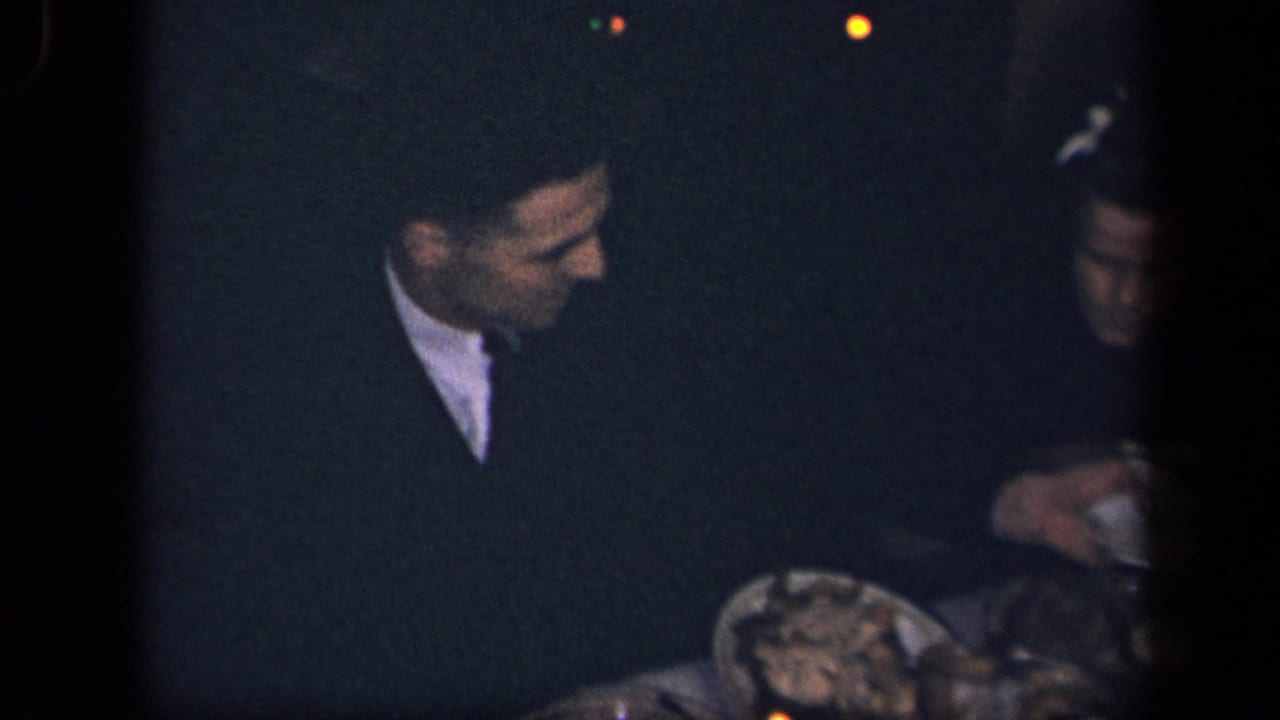 A man in dark clothing sits beside a woman at a low-lit dinner table in the 1942 Sebring, Ohio home movie.