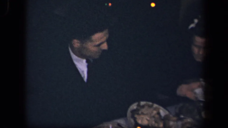 A man in dark clothing sits beside a woman at a low-lit dinner table in the 1942 Sebring, Ohio home movie.
