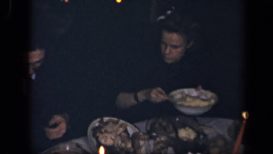 The woman sits at the 1942 Sebring, Ohio dinner table with serving dishes, plates, and a red candle visible in low light.