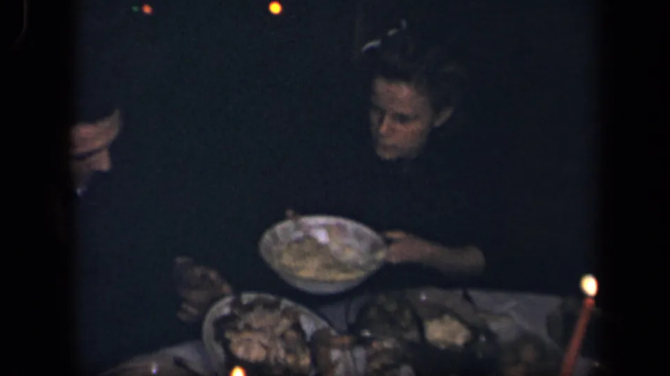 In Sebring, Ohio, 1942 home-movie footage, adults sit around a dim candle-lit table as food is served from shared dishes.