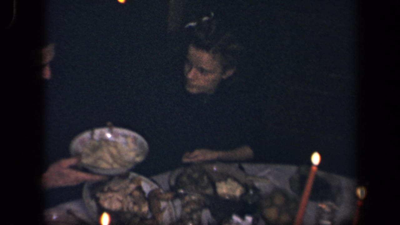 A hand offers a large serving bowl across a candle-lit dinner table.
