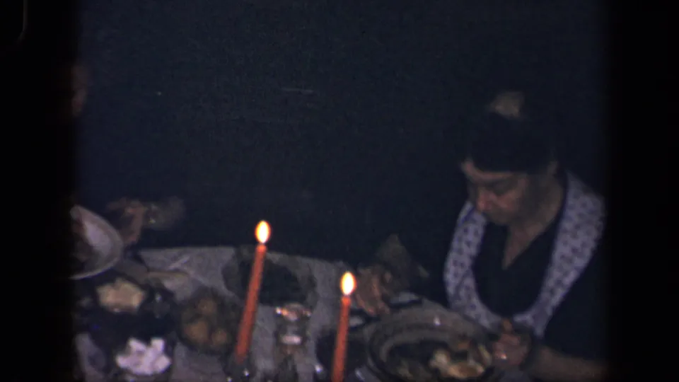 A woman in a patterned apron sits at the candle-lit dinner table in Sebring, Ohio, with food and tableware visible around her.